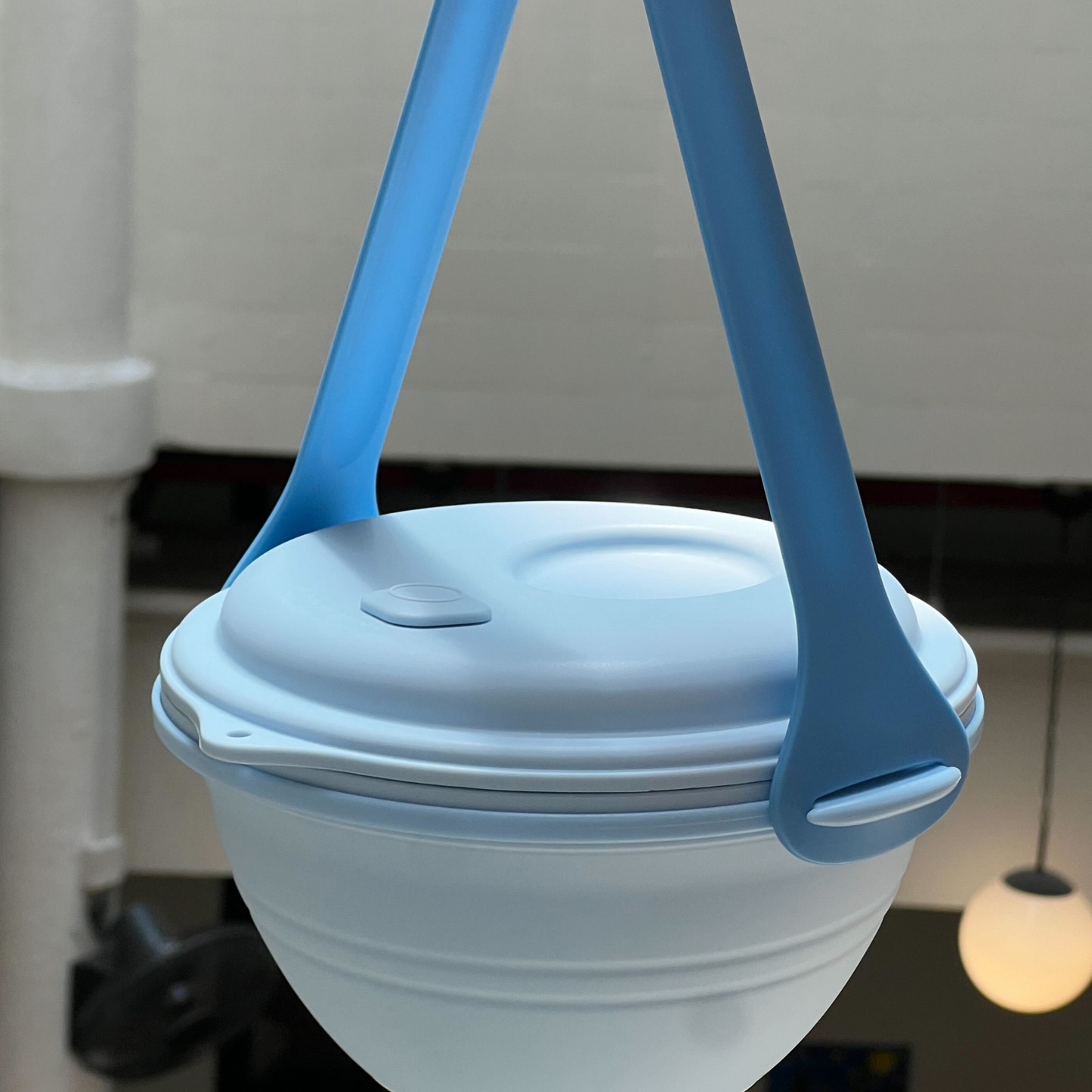 Collapsible silicone food container with blue handle on a blurred background